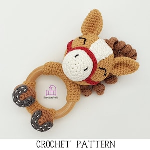 Peut inclure: Un hochet pour bébé fait à la main en crochet en forme de cheval. Le hochet présente un anneau en bois, des détails en crochet marron et blanc et un accent rouge. Le texte "CROCHET PATTERN" est au bas de l'image.