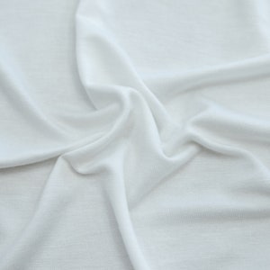 K&ouml;nnte beinhalten: Wei&szlig;er Stoff mit einer glatten, weichen Textur. Der Stoff ist zerknittert und gefaltet, wodurch ein strukturierter Hintergrund entsteht.