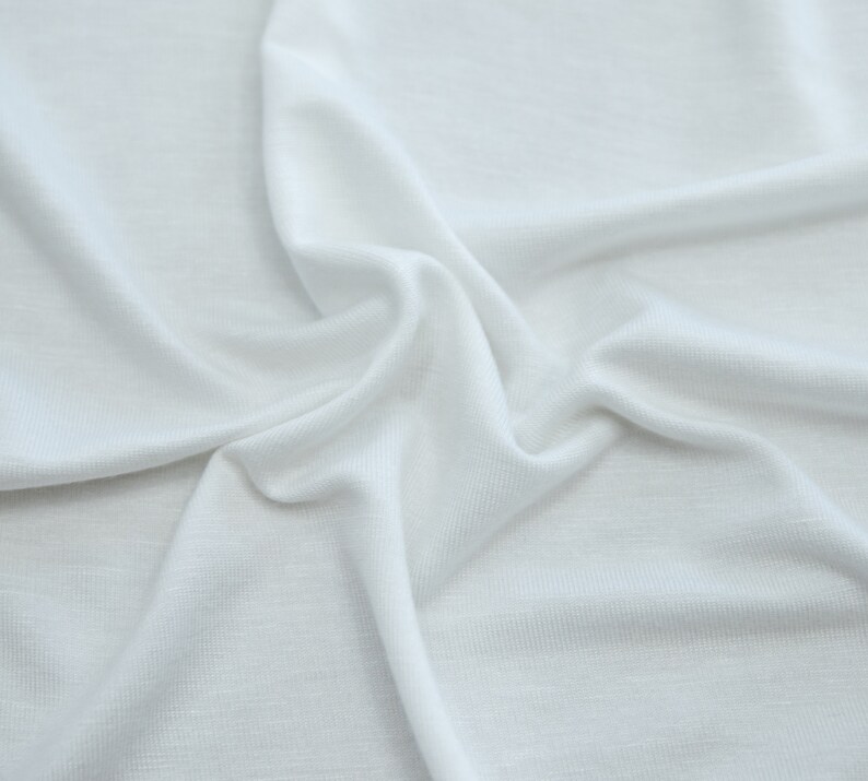 K&ouml;nnte beinhalten: Wei&szlig;er Stoff mit einer glatten, weichen Textur. Der Stoff ist zerknittert und gefaltet, wodurch ein strukturierter Hintergrund entsteht.