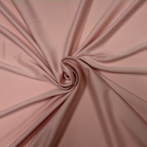 Puede incluir: Primer plano de una tela suave y lisa de color rosa claro. La tela est&aacute; drapeada y doblada, creando un patr&oacute;n de espiral.