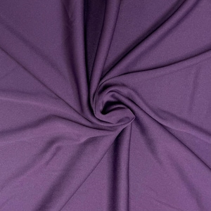 Puede incluir: Primer plano de una tela suave y morada con una textura lisa. La tela est&aacute; drapeada y doblada, creando un patr&oacute;n de remolino.