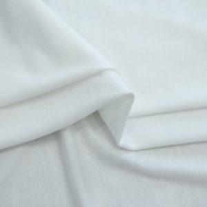 K&ouml;nnte beinhalten: Wei&szlig;er Stoff mit einer glatten, weichen Textur. Der Stoff ist so gefaltet, dass der Fall und die Flie&szlig;f&auml;higkeit des Materials sichtbar werden.