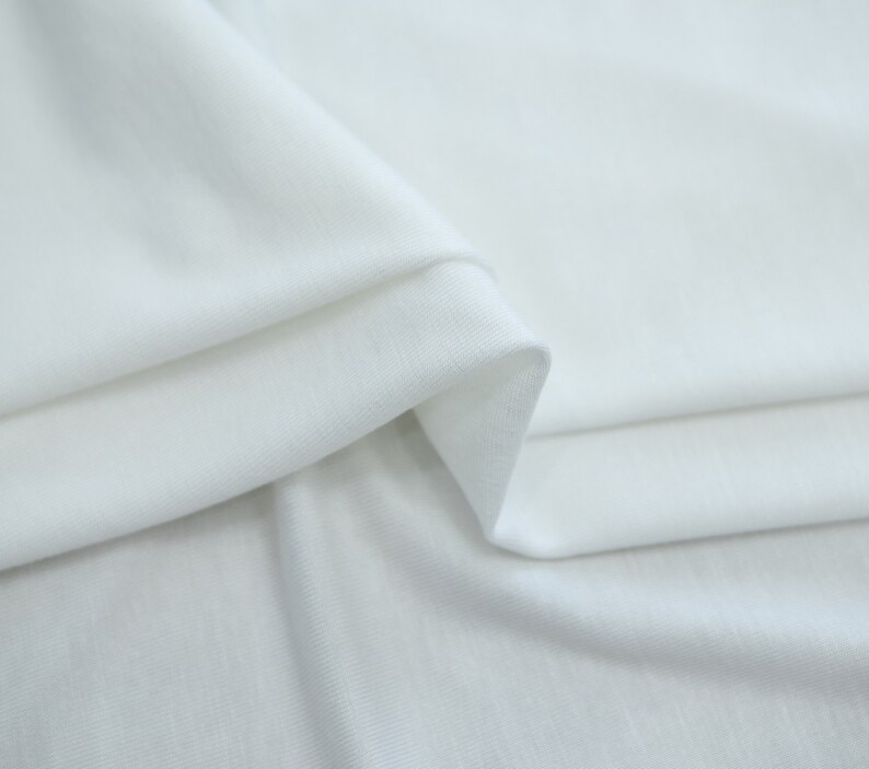 K&ouml;nnte beinhalten: Wei&szlig;er Stoff mit einer glatten, weichen Textur. Der Stoff ist so gefaltet, dass der Fall und die Flie&szlig;f&auml;higkeit des Materials sichtbar werden.