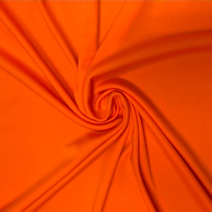 Puede incluir: Primer plano de una tela de color naranja brillante con una textura lisa. La tela est&aacute; doblada y drapeada, creando pliegues y curvas suaves.