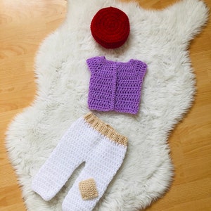 May include: A crocheted outfit for a baby, including a purple vest, white pants with a tan patch, and a red hat.