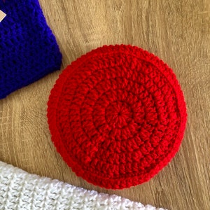May include: A red crocheted round cushion with a circular pattern. The cushion is made of yarn and has a soft, textured surface.