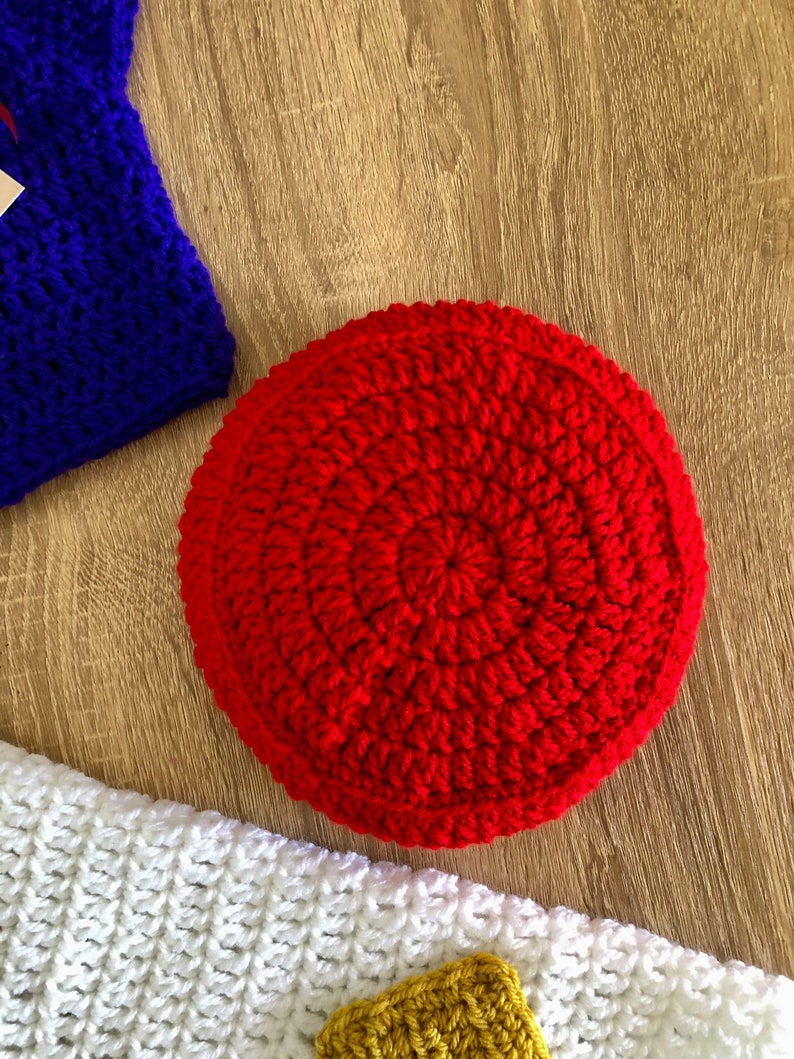 May include: A red crocheted round cushion with a circular pattern. The cushion is made of yarn and has a soft, textured surface.