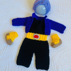 May include: A crocheted baby outfit in black, blue, and yellow, with a matching wig. The outfit includes a jumpsuit, a jacket, and booties.