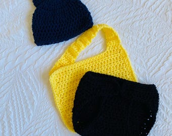 May include: A set of crocheted baby clothes in black and yellow. The set includes a hat with two pointy ears, a bib, and a pair of pants.