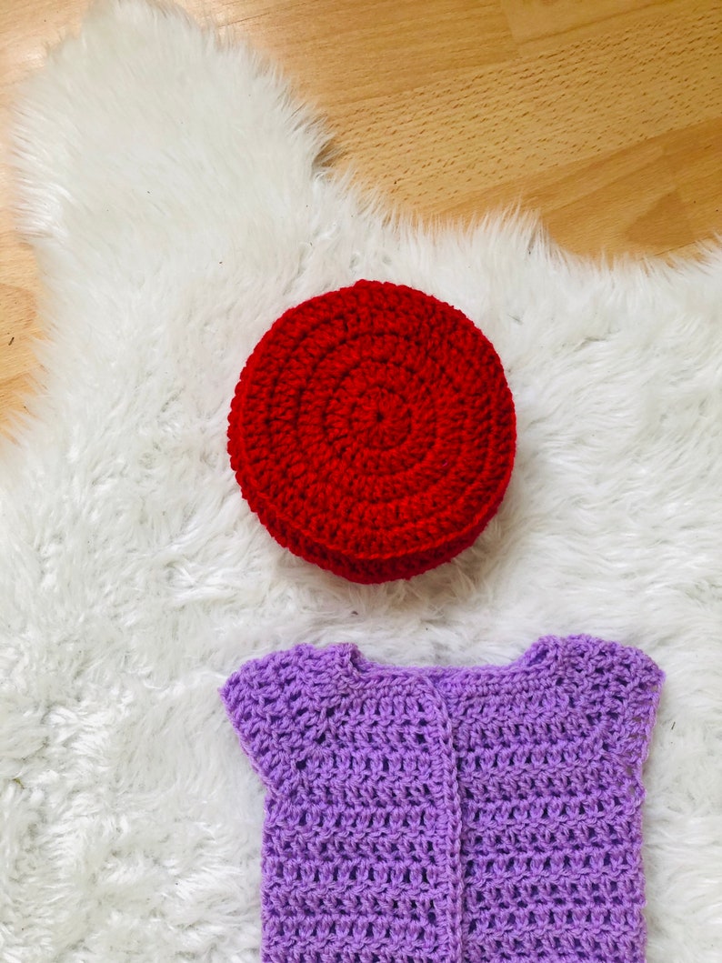 May include: A purple crocheted baby cardigan with short sleeves and a red crocheted hat.