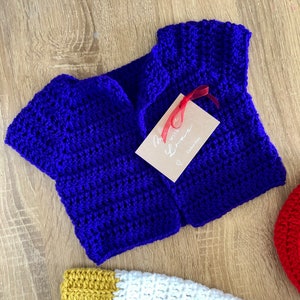 May include: A blue crocheted baby cardigan with a tag that says "Made with Love" and a red ribbon.
