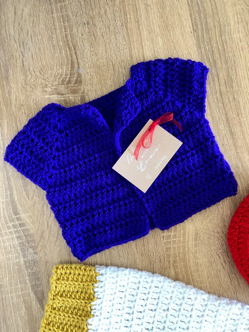 May include: A blue crocheted baby cardigan with a tag that says "Made with Love" and a red ribbon.