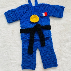 Peut inclure: Tenue de karaté en crochet bleu pour bébé avec une ceinture noire, une médaille jaune et un écusson rouge et blanc.