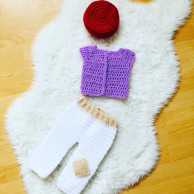 May include: A crocheted outfit for a baby, including a purple vest, white pants with a tan trim, and a red hat.