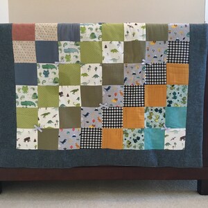 May include: A green, blue, and orange patchwork baby quilt with a dinosaur theme. The quilt is made of various fabrics with different patterns, including polka dots, stripes, and checkered patterns. The quilt is displayed on a crib.