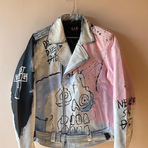 K&ouml;nnte beinhalten: Eine wei&szlig;e, rosa und blaue Lederjacke mit einem Totenkopf-Motiv und dem Text "DIE DIE DIE" und "NEVER SAY DIE", der darauf gemalt ist. Die Jacke hat einen Rei&szlig;verschluss und einen G&uuml;rtel an der Taille.