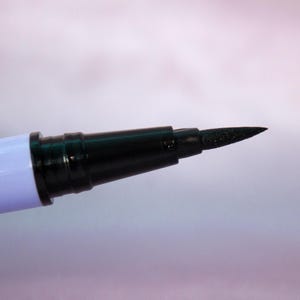 Puede incluir: Un delineador de ojos líquido negro con una punta fina. El bolígrafo tiene un cuerpo azul claro.