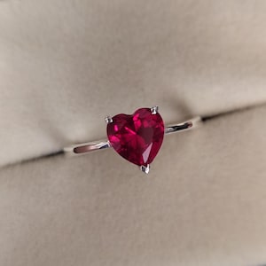 Könnte beinhalten: Ein silberner Ring mit einem herzförmigen Rubin.