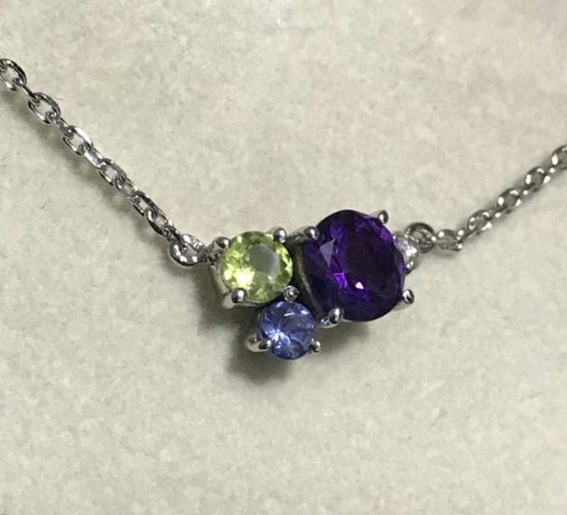 May include: A silver chain necklace with a cluster of three gemstones. The largest gemstone is a deep purple amethyst, surrounded by a smaller light green peridot and a tiny blue topaz.