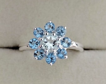 May include: A silver ring with a cluster of blue topaz gemstones set in a flower shape.
