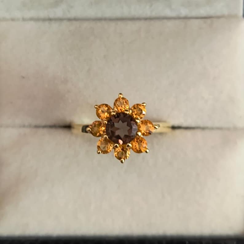 May include: A gold ring with a brown gemstone surrounded by smaller orange gemstones in a flower shape.