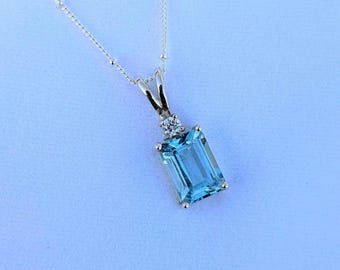 Könnte beinhalten: Eine silberne Halskette mit einem rechteckigen, hellblauen Edelsteinanhänger. Der Anhänger ist mit einem kleinen Diamanten verziert und hängt an einer zarten Kette. Der Edelstein ist etwa 2 cm lang.