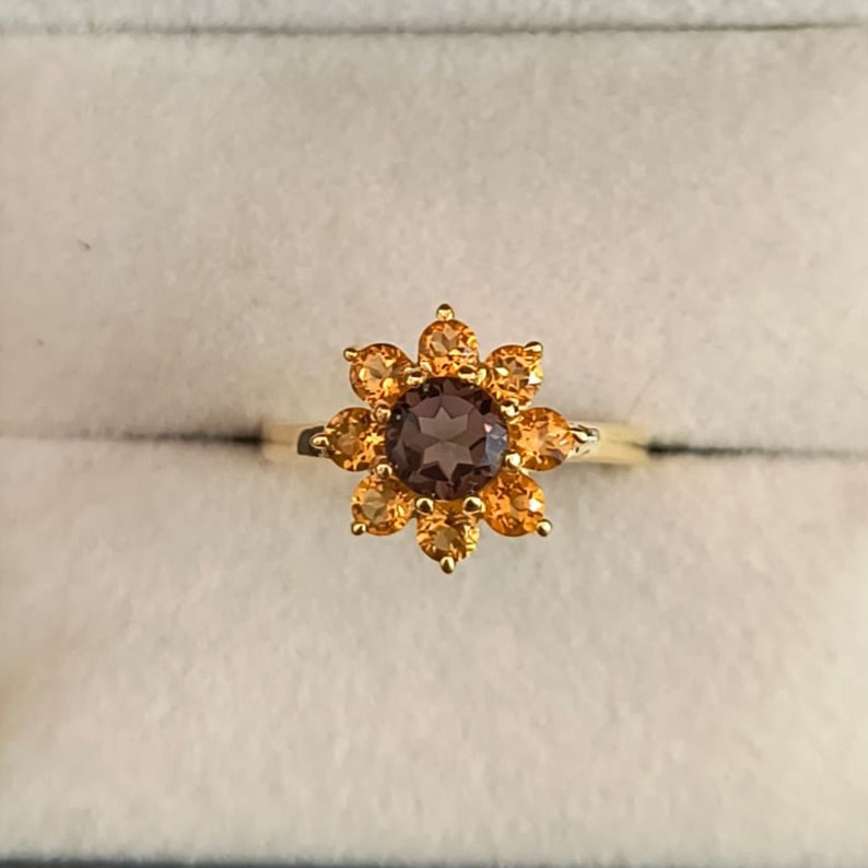 May include: A gold ring with a brown gemstone surrounded by smaller orange gemstones in a flower shape.