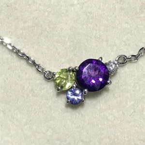 May include: A silver chain necklace with a cluster of gemstones. The cluster includes a large purple amethyst, a smaller green peridot, and a tiny blue sapphire.