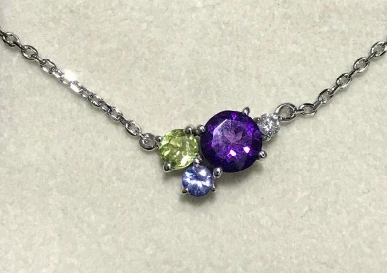 May include: A silver chain necklace with a cluster of gemstones. The cluster includes a large purple amethyst, a smaller green peridot, and a tiny blue sapphire.