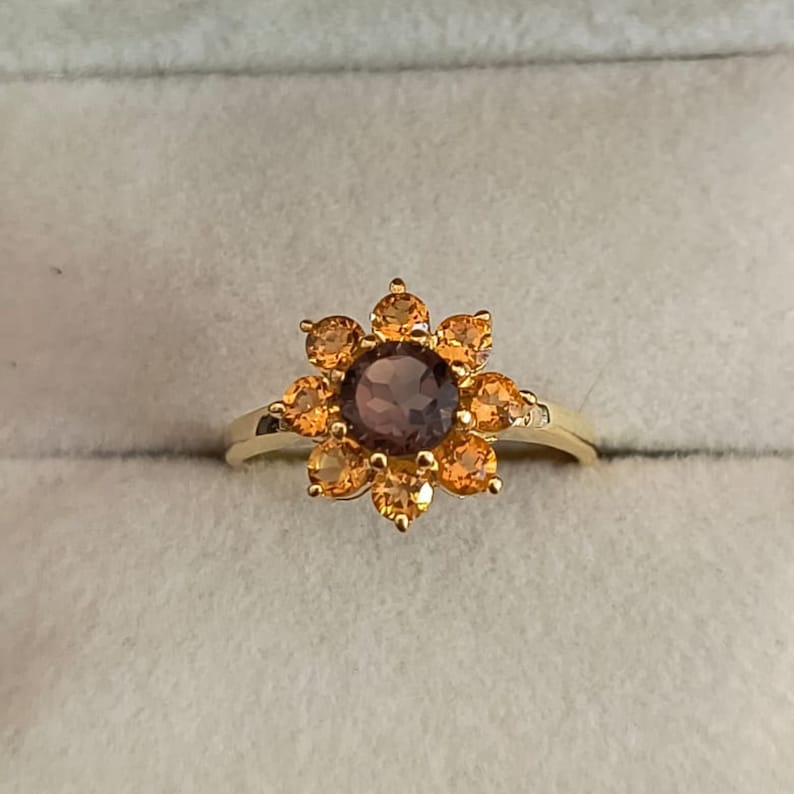 May include: A gold ring with a brown gemstone surrounded by smaller orange gemstones in a flower shape.