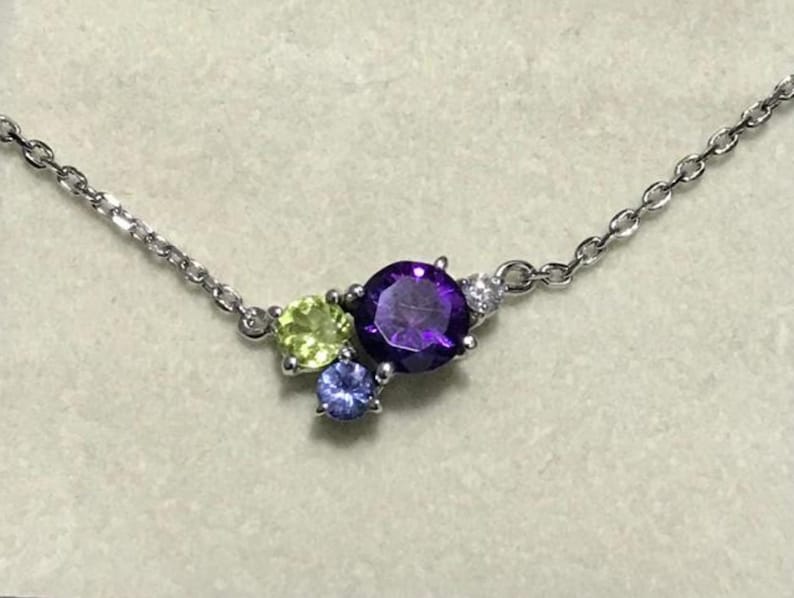 May include: A silver chain necklace with a cluster of three gemstones. The largest gemstone is a round, purple amethyst. The other two gemstones are smaller and round, one is green and one is blue.