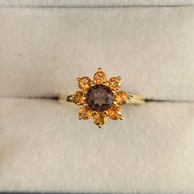 May include: A gold ring with a brown gemstone surrounded by smaller orange gemstones in a flower shape.