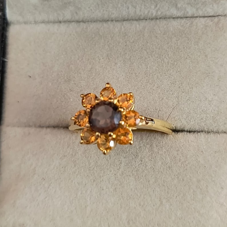 May include: A gold ring with a brown gemstone surrounded by smaller orange gemstones in a flower shape.