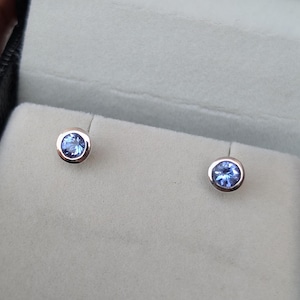 Pode incluir: Um par de brincos de prata com uma gema azul claro em cada um. Os brincos são montados em uma configuração simples e redonda.
