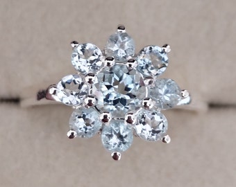 May include: A silver ring with a cluster of light blue aquamarine gemstones set in a flower shape.
