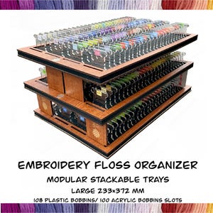 May include: A wooden embroidery floss organizer with black trim and multiple levels. The organizer has clear plastic bobbins filled with colorful thread. Text on the image reads "EMBROIDERY FLOSS ORGANIZER, MODULAR STACKABLE TRAYS, LARGE 233x372 MM, 108 PLASTIC BOBBINS/ 100 ACRYLIC BOBBINS SLOTS."
