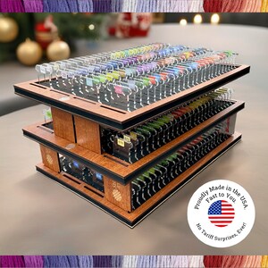 May include: A three-tiered wooden organizer with multiple compartments, filled with colorful thread spools. Each spool is labeled with a number. The organizer has a black trim and a circular sticker that says "Proudly Made in the USA. Fast to You. No Tariff Surprises, Ever!"