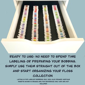May include: A white drawer with a black foam insert for organizing embroidery floss. The drawer is full of labeled bobbins of floss in various colors. The text on the drawer reads "READY TO USE: NO NEED TO SPEND TIME LABELING OR PREPARING YOUR BOBBINS. SIMPLY USE THEM STRAIGHT OUT OF THE BOX AND START ORGANIZING YOUR FLOSS COLLECTION".