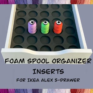 May include: A white drawer with a black foam insert designed to hold spools of thread. Three spools of thread in purple, green, and red are visible. Text on the drawer reads "FOAM SPOOL ORGANIZER INSERTS FOR IKEA ALEX 5-DRAWER."