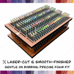 May include: A wooden thread organizer with multiple slots, holding numerous bobbins with colored thread. The organizer has a laser-cut design and smooth finish. The text at the bottom reads "LASER-CUT & SMOOTH-FINISHED GENTLE ON BOBBINS; PRECISE FOAM FIT."