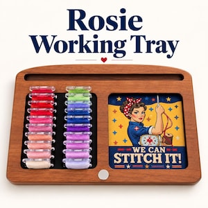 May include: A wooden working tray labeled Rosie Working Tray featuring two columns of colorful embroidery floss bobbins and a square graphic insert depicting a person with a red headband holding a needle with the text We Can Stitch It.