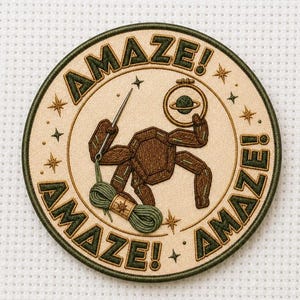 May include: A circular embroidered patch with a cream background and dark green border. It features a brown geometric creature holding a needle and a skein of green yarn, with the text AMAZE! repeated around the edge and small star accents.