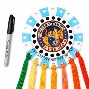 May include: A circular white and light blue striped embroidery floss organizer with a central graphic of a woman in a red headband and blue shirt, featuring the text WE CAN STITCH IT! USA 250. Six colorful embroidery threads are attached, and a black marker.