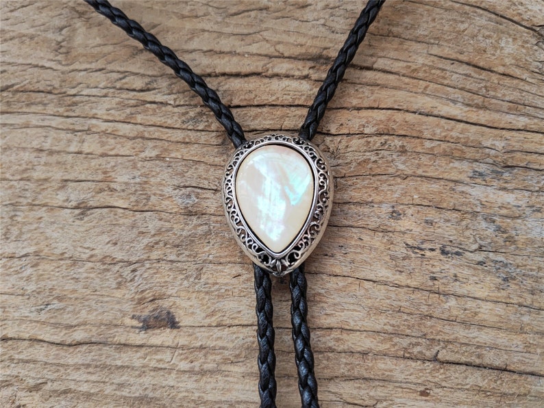 May include: A black leather bolo tie with a silver and white pearlescent stone pendant.