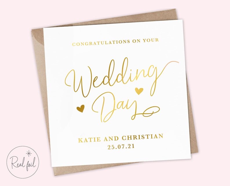 K&ouml;nnte beinhalten: Eine wei&szlig;e Karte mit goldenen Schriftz&uuml;gen, die "Herzlichen Gl&uuml;ckwunsch zu Ihrem Hochzeitstag" mit zwei kleinen goldenen Herzen sagen. Unter dem Text steht "Katie und Christian 25.07.21" in goldenen Schriftz&uuml;gen.