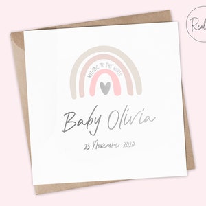 Puede incluir: Una tarjeta blanca con un arco&iacute;ris rosa y beige con un coraz&oacute;n gris en el centro. El texto "Bienvenido al mundo" est&aacute; escrito en el arco&iacute;ris. Debajo del arco&iacute;ris est&aacute; el texto "Baby Olivia" y la fecha "23 de noviembre de 2020".