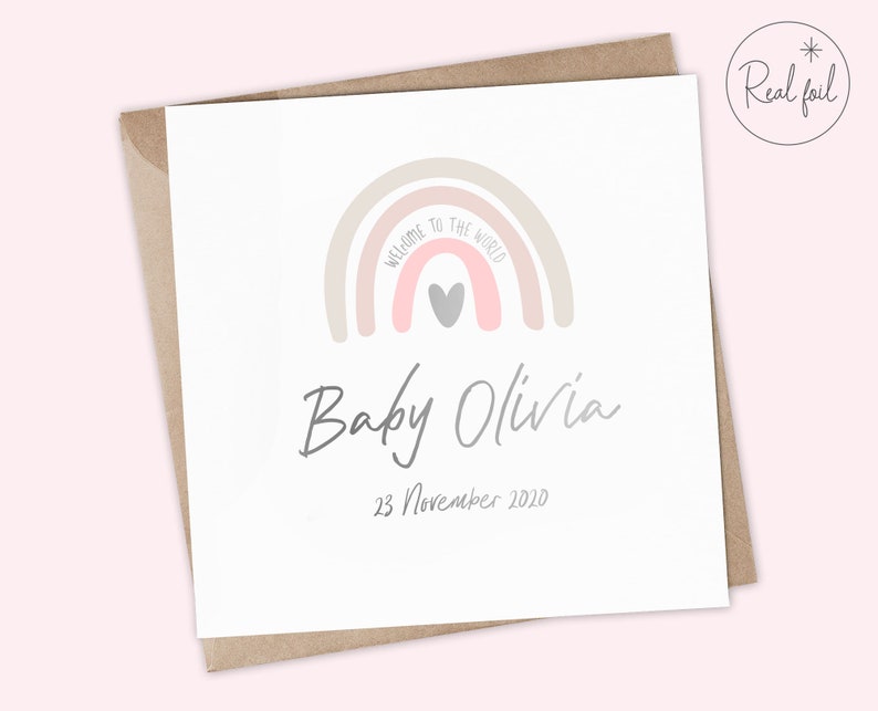 Puede incluir: Una tarjeta blanca con un arco&iacute;ris rosa y beige con un coraz&oacute;n gris en el centro. El texto "Bienvenido al mundo" est&aacute; escrito en el arco&iacute;ris. Debajo del arco&iacute;ris est&aacute; el texto "Baby Olivia" y la fecha "23 de noviembre de 2020".