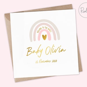 Puede incluir: Una tarjeta blanca con un arco&iacute;ris rosa y beige con un coraz&oacute;n dorado en el centro. El texto "Bienvenido al mundo" est&aacute; escrito en el arco&iacute;ris. Debajo del arco&iacute;ris est&aacute; el texto "Baby Olivia" en escritura dorada y la fecha "23 de noviembre de 2020" en dorado.