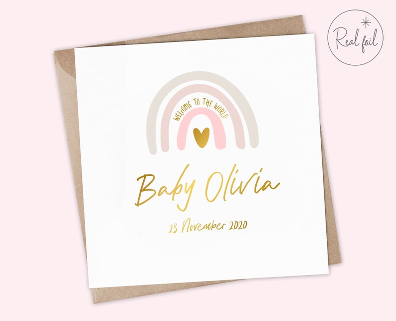 Puede incluir: Una tarjeta blanca con un arco&iacute;ris rosa y beige con un coraz&oacute;n dorado en el centro. El texto "Bienvenido al mundo" est&aacute; escrito en el arco&iacute;ris. Debajo del arco&iacute;ris est&aacute; el texto "Baby Olivia" en escritura dorada y la fecha "23 de noviembre de 2020" en dorado.