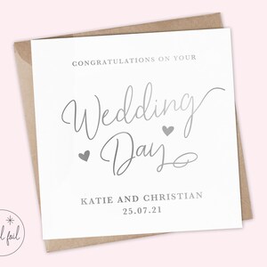 K&ouml;nnte beinhalten: Eine wei&szlig;e Hochzeitskarte mit silberner Folienbeschriftung, auf der "Herzlichen Gl&uuml;ckwunsch zu Ihrem Hochzeitstag" mit zwei kleinen Herzen steht. Die Karte enth&auml;lt auch die Namen Katie und Christian sowie das Datum 25.07.21.